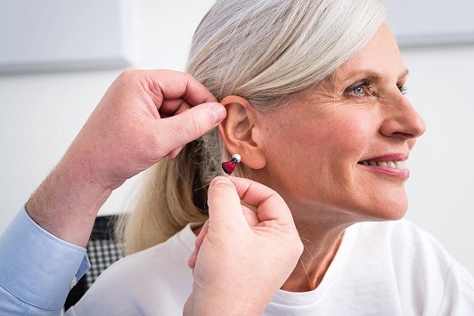 Ältere Frau erhält von einem Hörakustiker ein modernes Hörgerät ins Ohr eingesetzt.